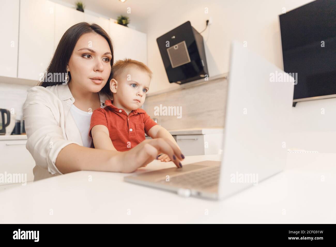 Business mom is using laptop, woman spending time with her boy baby home Stock Photo