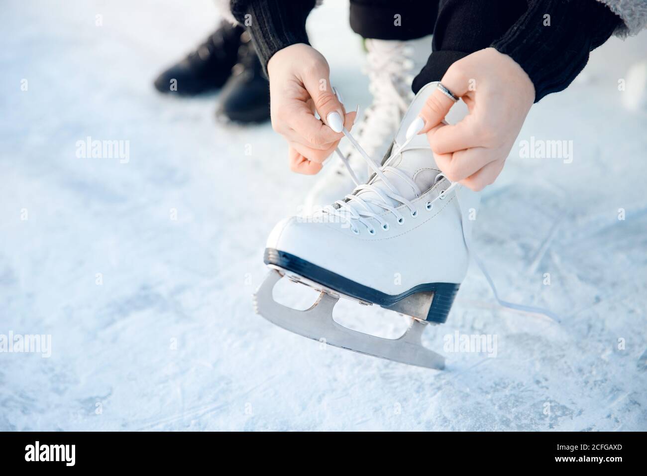 Girl ties shoelaces on white figure skates for ice rink in winter