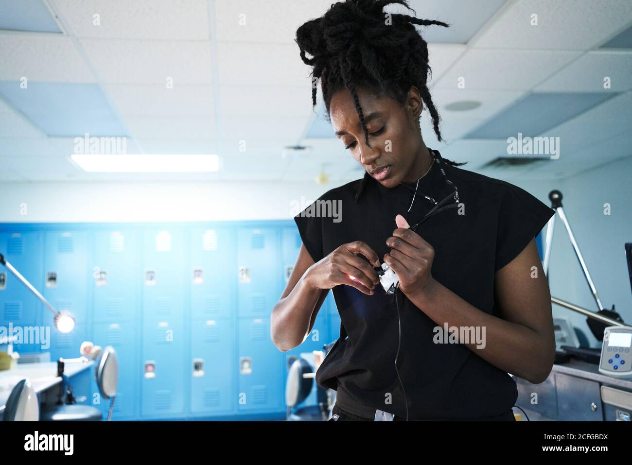 African American female specialist with dreadlocks adjusting and turning on lamp of binocular glasses while working in contemporary laboratory Stock Photo