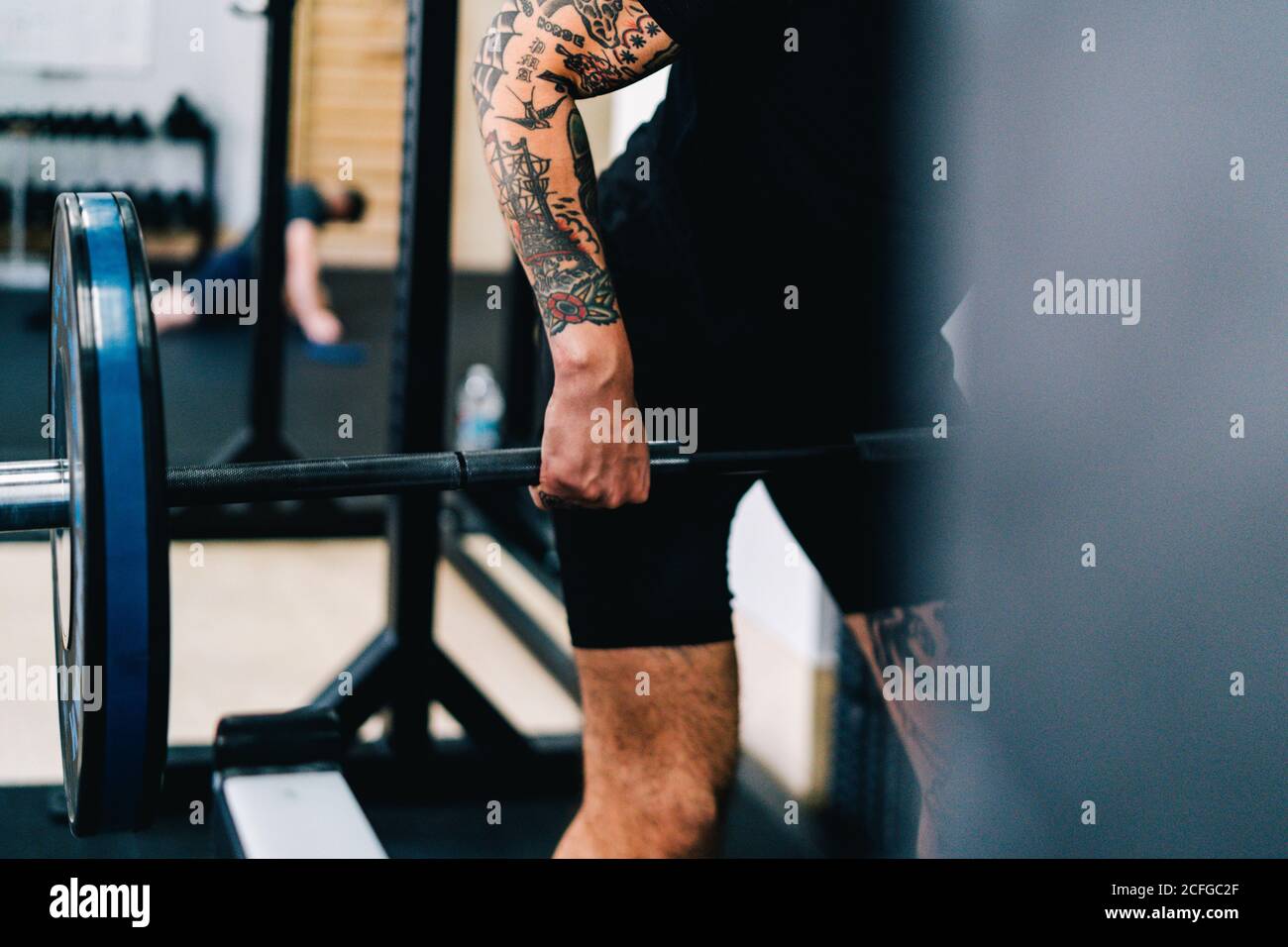 Crop tattooed sportsman in t shirt and shorts practicing dead lift while training in modern gym Stock Photo