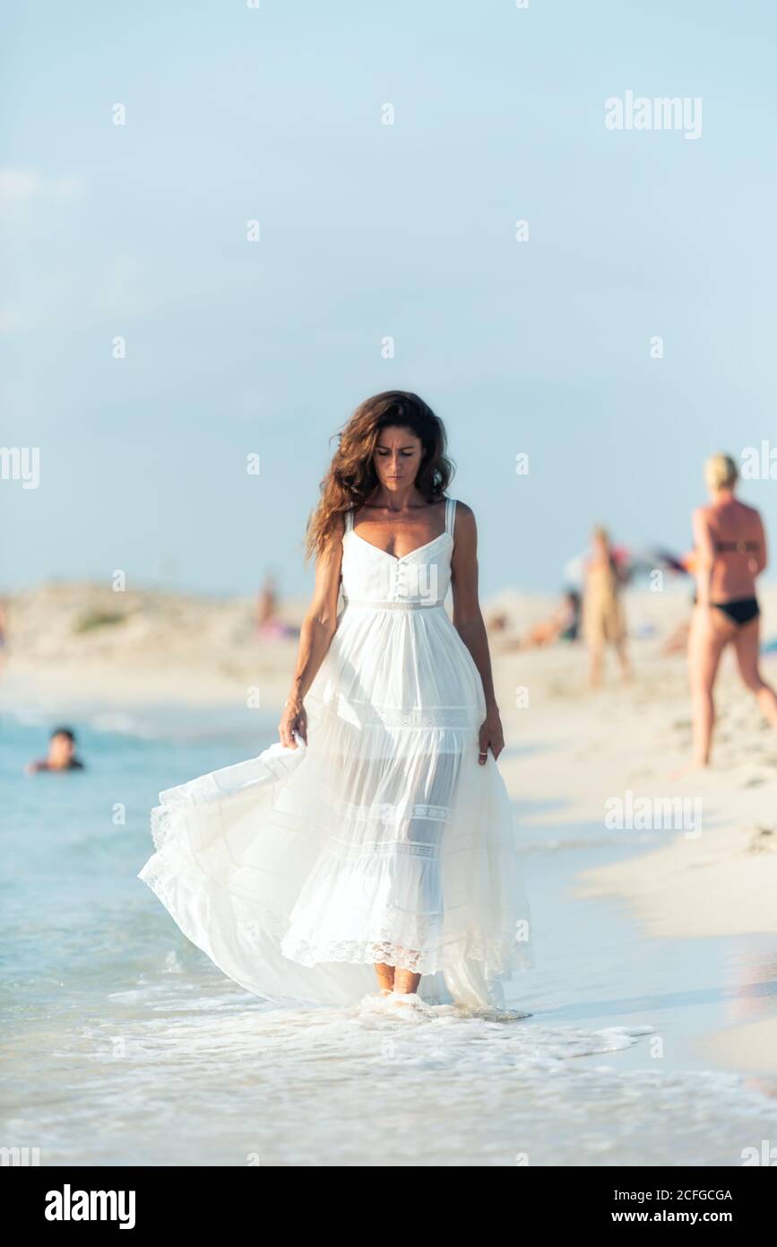 Woman in light white dress walking on beach and looking down Stock Photo -  Alamy