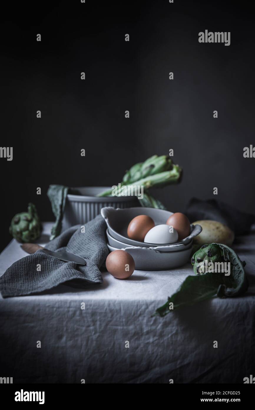 Eggs and different herbs in bowls placed on rustic table Stock Photo