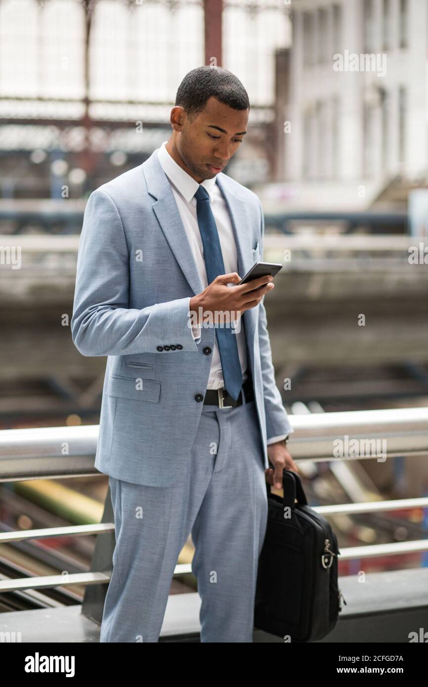 Serious black man in trendy suit using smartphone Stock Photo