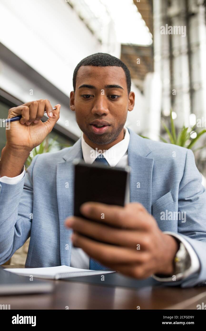 man using smartphone sitting at table with a pen in hand Stock Photo