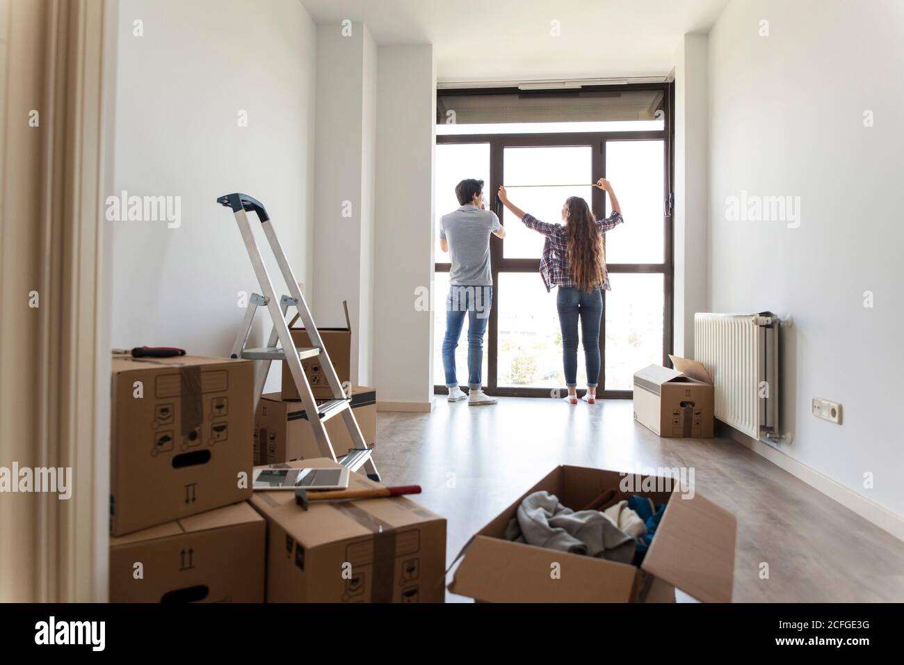 Young male and female measuring window with linear tape in apartment ...