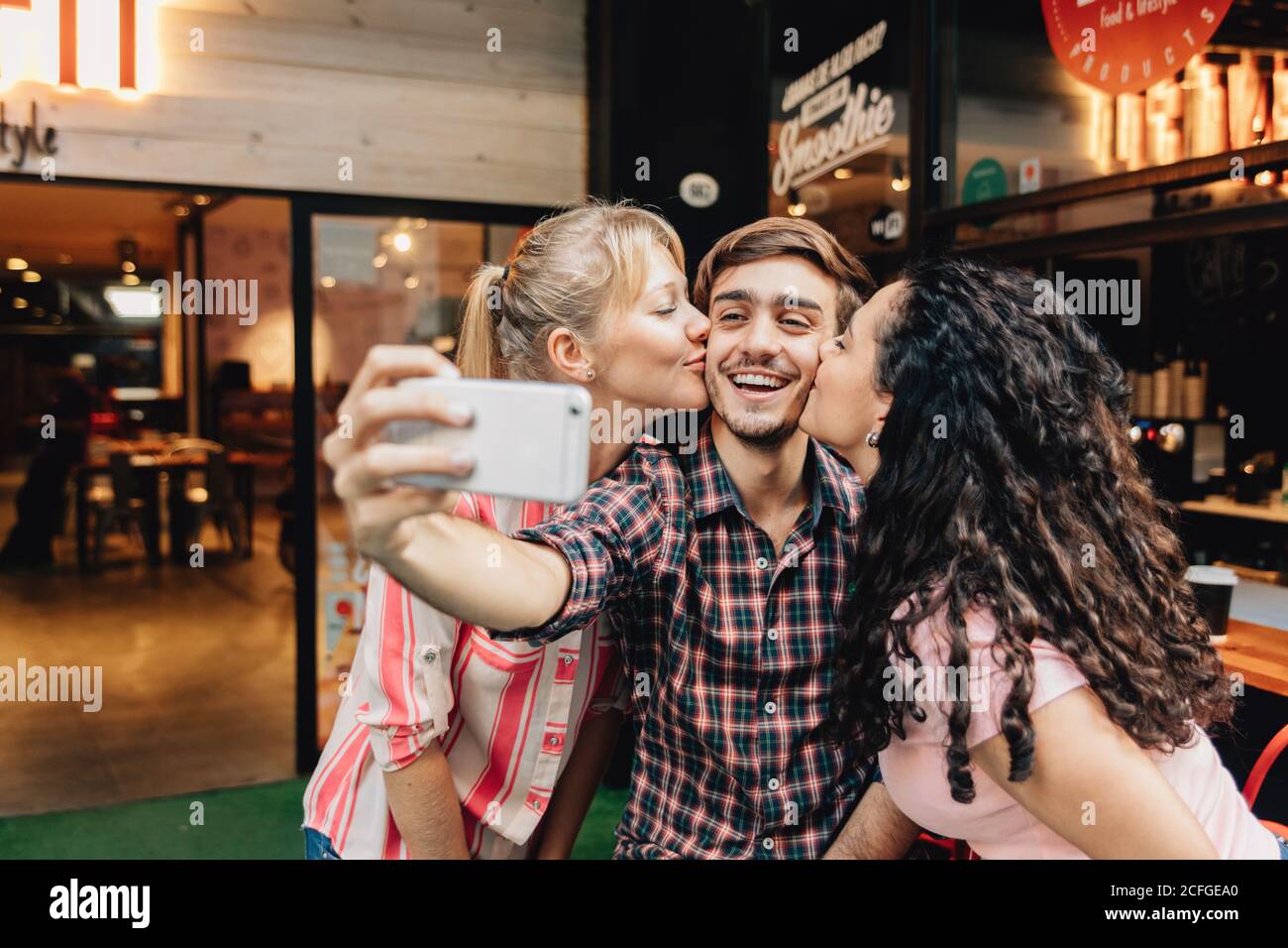 girls kissing a young man taking a selfie Stock Photo
