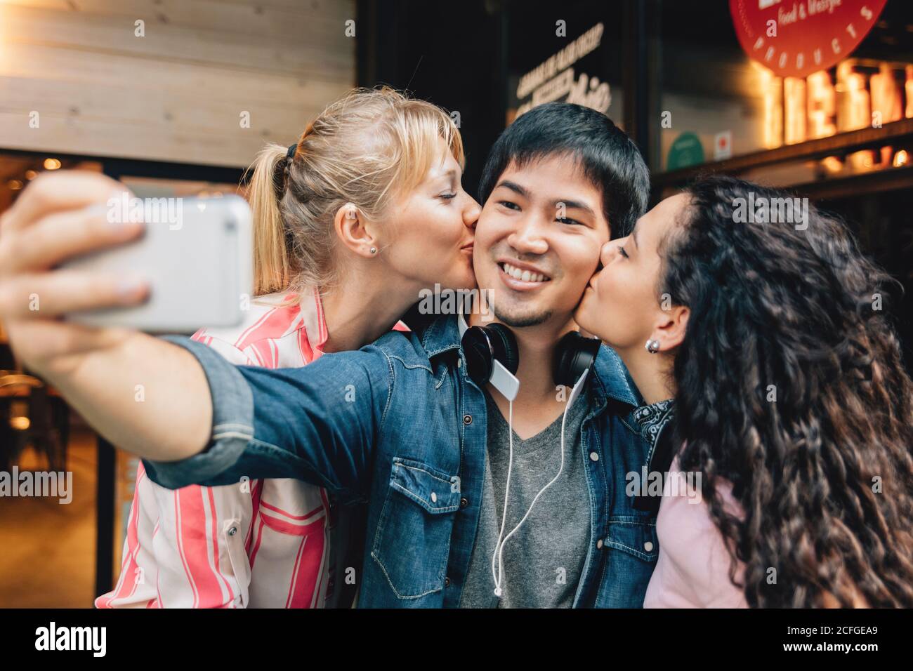 girls kissing a young man taking a selfie Stock Photo