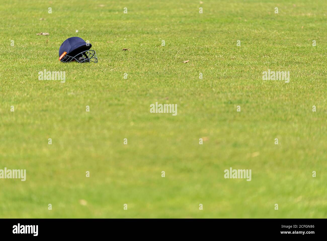 Cricket helmet on ground in Chalkwell Park, Westcliff on Sea, Southend, Essex, UK. Batsman's headgear isolated on grass pitch. Discarded Stock Photo