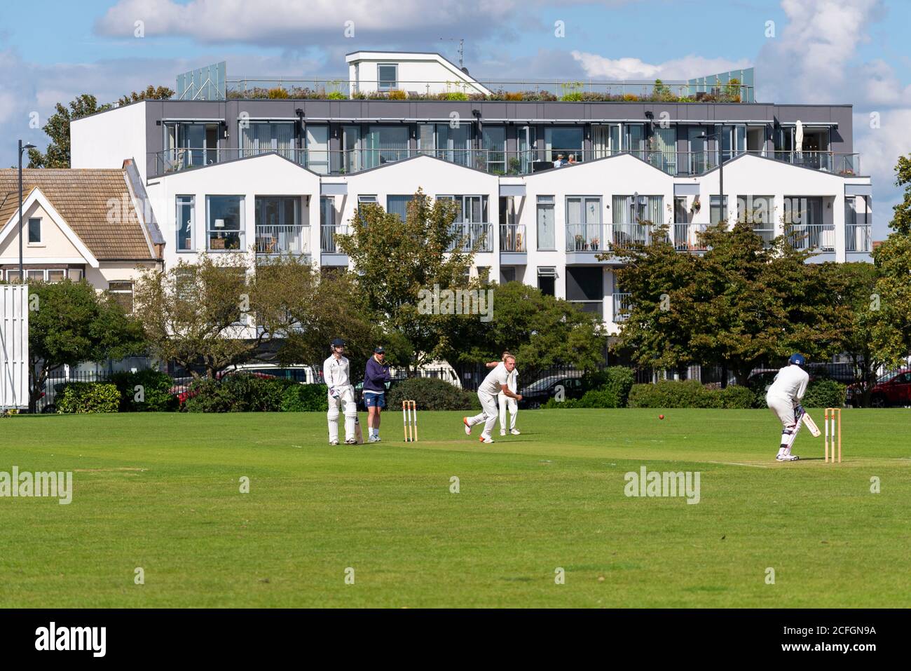 Cricket being played in Chalkwell Park, Westcliff on Sea, Southend, Essex, UK. Flats, apartments overlooking the park, London Road. Bowler bowling Stock Photo