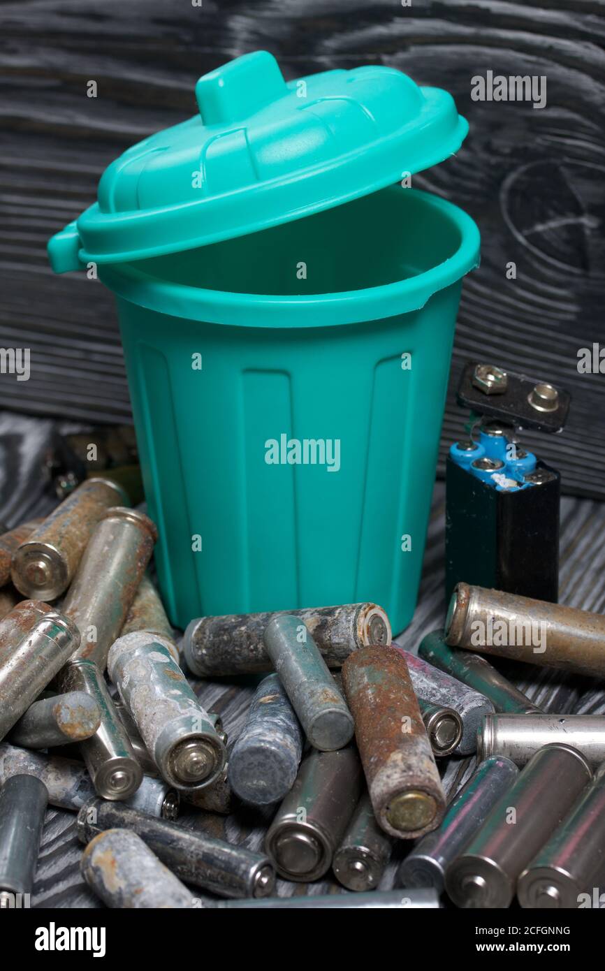 Corroded used batteries. Nearby is a trash can. On pine boards