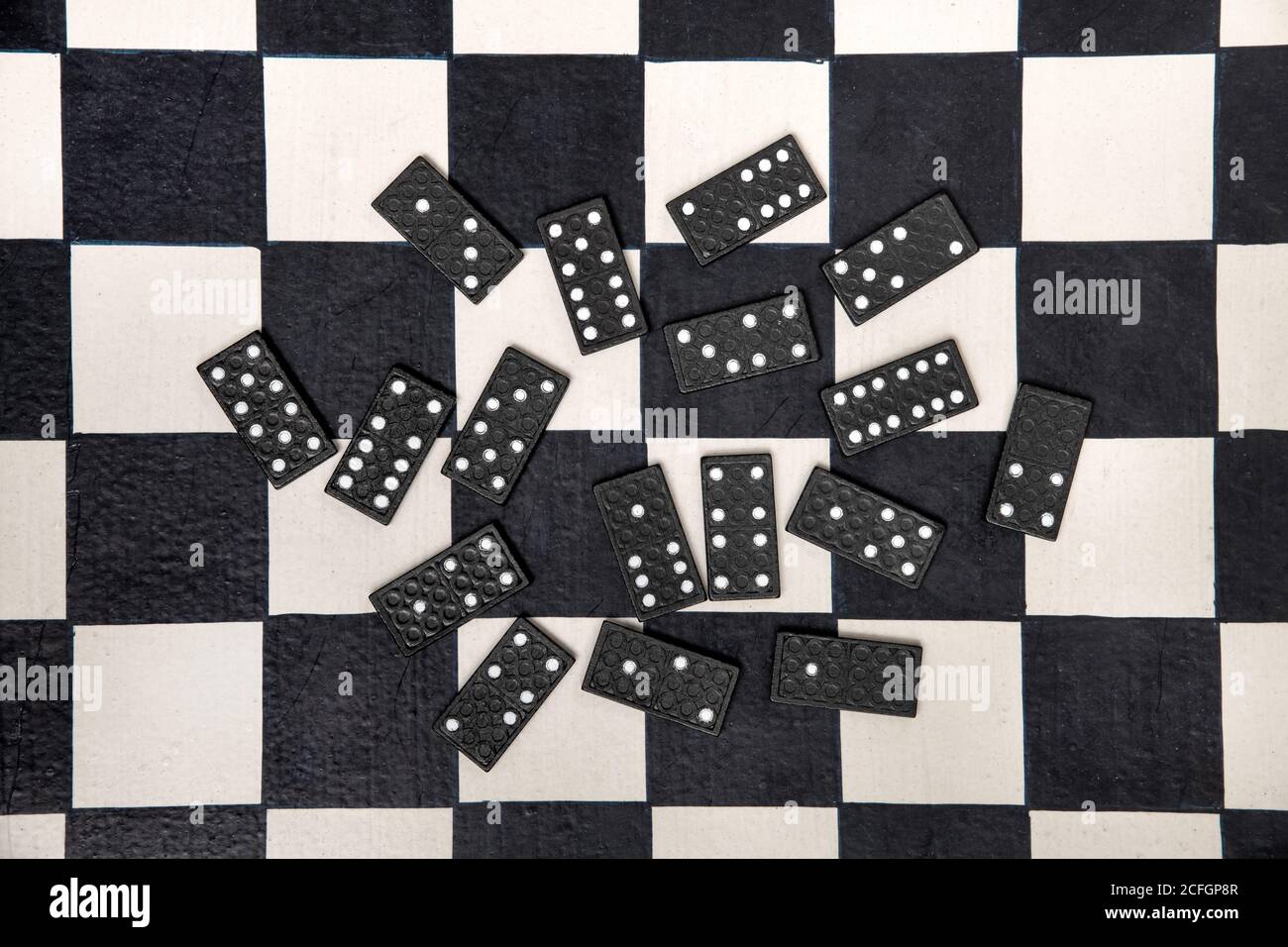 Randomly scattered black domino tiles on a black and white chessboard viewed from above in a concept of personal entertainment Stock Photo