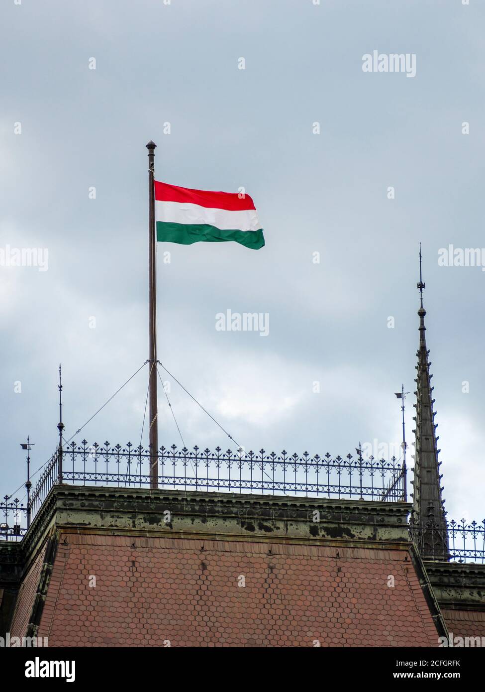 Hungarian Flag flying above Parliament: A large hungarian flag flies taughtly in the wind high above the massive Hungarian Parliament buildings in Central Budapest. Stock Photo