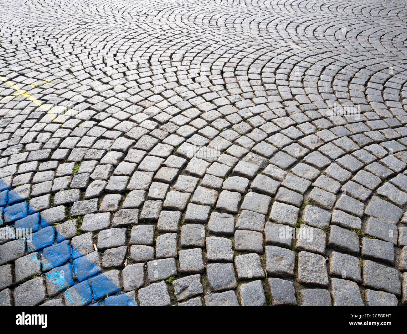 Concentric Cobble Curves: A series of concentric circles form a pattern on a cobbled street in the castle district in Prague. Pavement markings brighten up some stones. Grass sprouts. Stock Photo