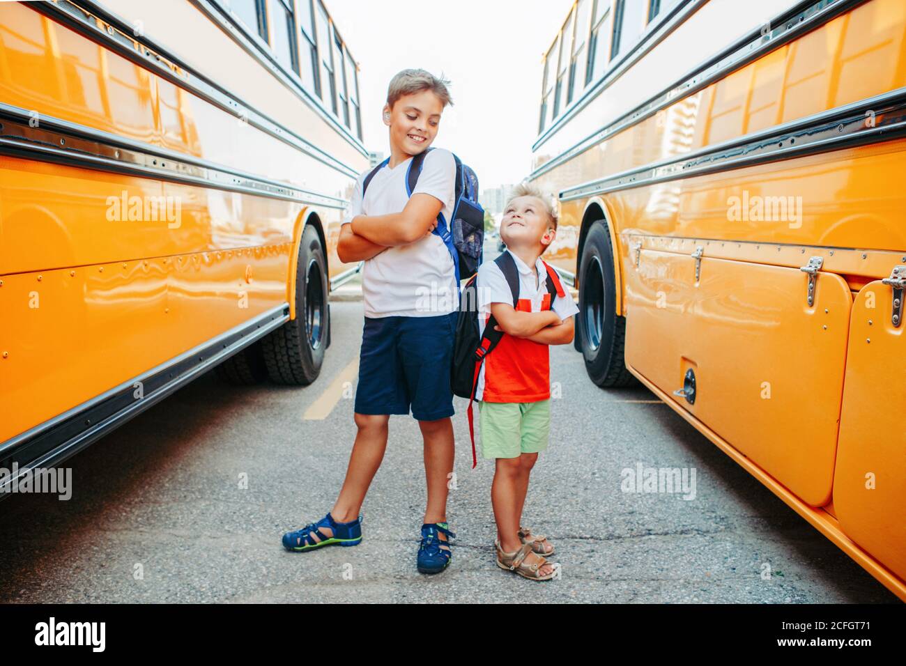 Happy Caucasian brothers students near yellow school bus. Smiling kids going back to school in September. Education system and learning. Support and f Stock Photo