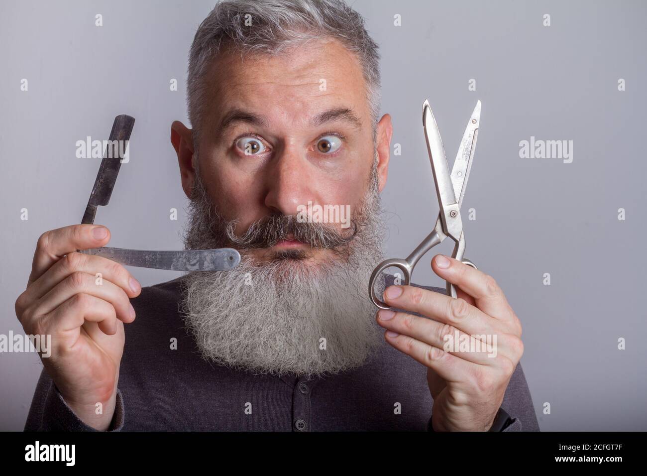 Portrait of mature bearded man with retro razor and scissors, barbershop concept, selective focus Stock Photo