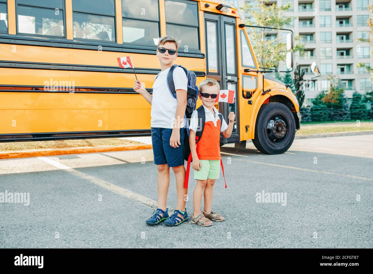 Caucasian boys students holding waving Canadian flag. Students kids near yellow school bus in Canada. Education and back to school in September. Proud Stock Photo
