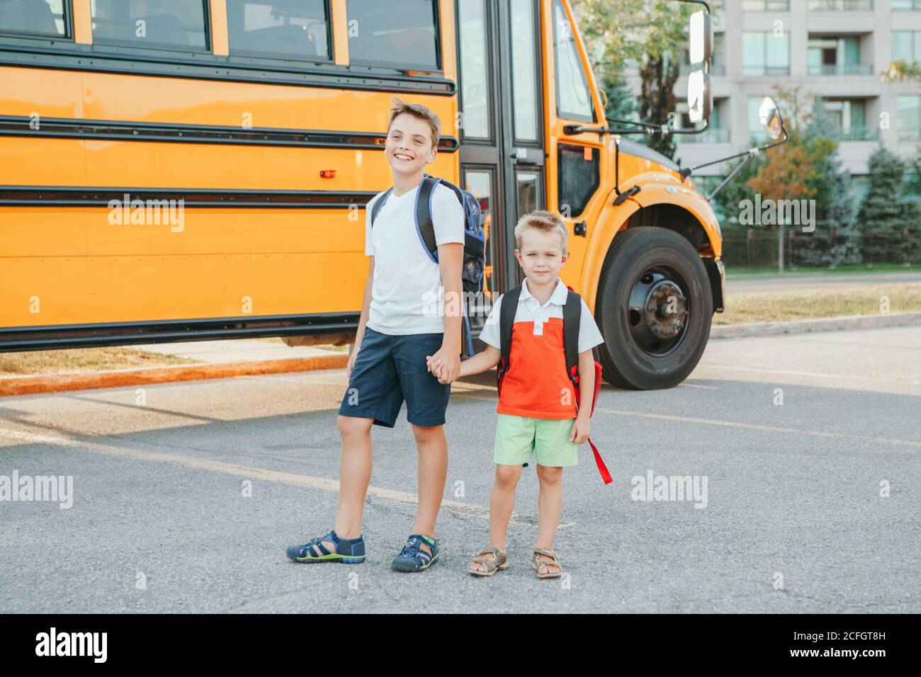 Happy Caucasian brothers students near yellow school bus. Smiling kids holding hands and going back to school in September. Education system and learn Stock Photo