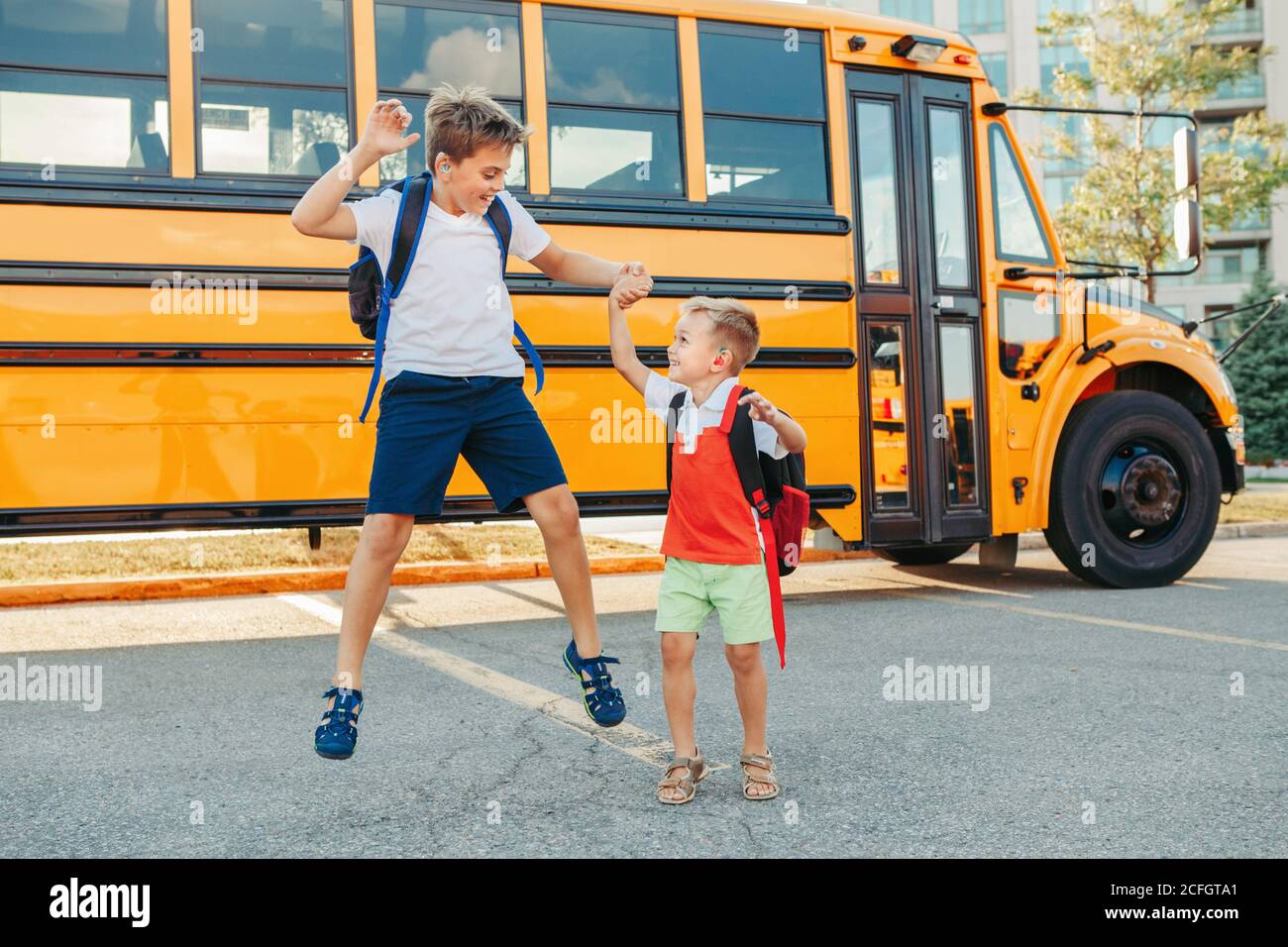Happy Caucasian brothers students jumping near yellow school bus