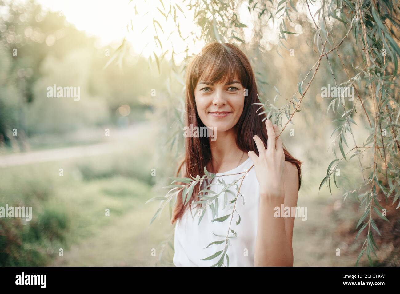 Beautiful happy smiling middle age young Caucasian woman with long dark brown red hair. Casual style real woman female in long white dress outdoor Stock Photo