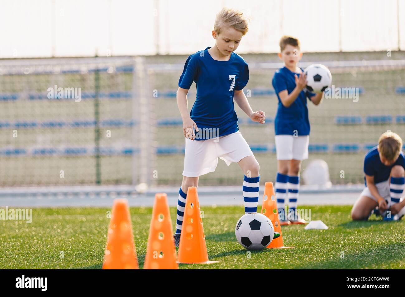 Young boys kicking soccer ball on training. Children practicing football on school grass pitch. Happy blonde boy running after soccer ball and trainin Stock Photo