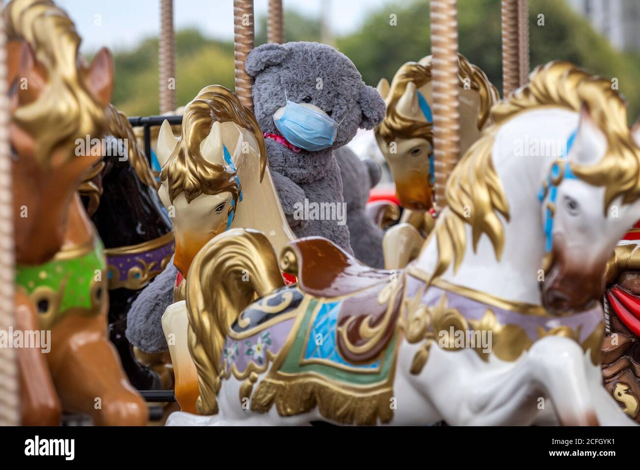 A teddy bear toy wearing a protective mask seats on a carousel horse in a city during the restrictions with the novel coronavirus COIVD-19 pandemic Stock Photo