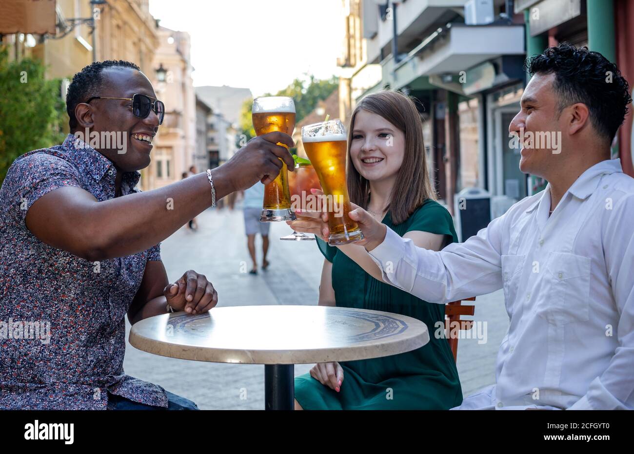 Multiracial group of friends drinking and toasting at street terrace of the cafe. Friendship concept with young multi ethnic people enjoying time toge Stock Photo