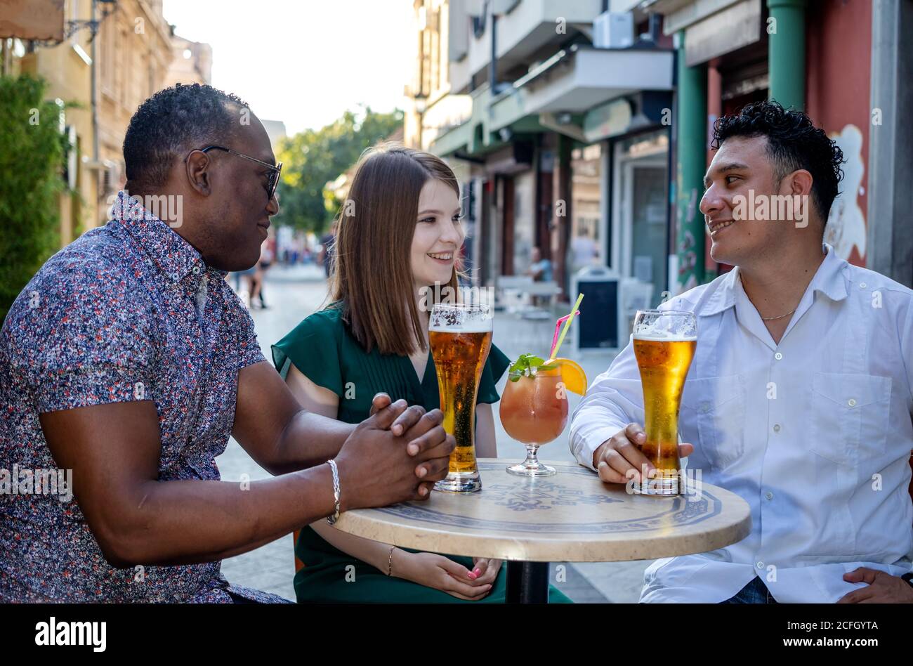 Multiracial couple on a date at a street terrace of the cafe. Third man looking at the woman. Concept of jealousy. Selective focus. Stock Photo