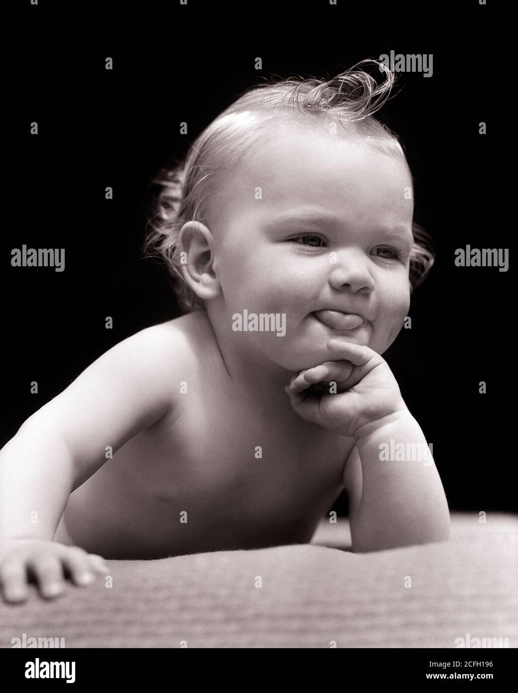 1930s CUTE ENGAGING BLOND BABY GIRL WITH ATTITUDE LYING ON BELLY RESTING CHIN ON HAND POLITELY STICKING OUT HER TONGUE - b17101 HAR001 HARS CHIN GESTURING EXPRESSIONS B&W RESTING HUMOROUS COMICAL STICKING GESTURES COMEDY PLEASANT AGREEABLE CHARMING JUVENILES LOVABLE PLEASING ADORABLE APPEALING BABY GIRL BLACK AND WHITE CAUCASIAN ETHNICITY HAR001 OLD FASHIONED Stock Photo