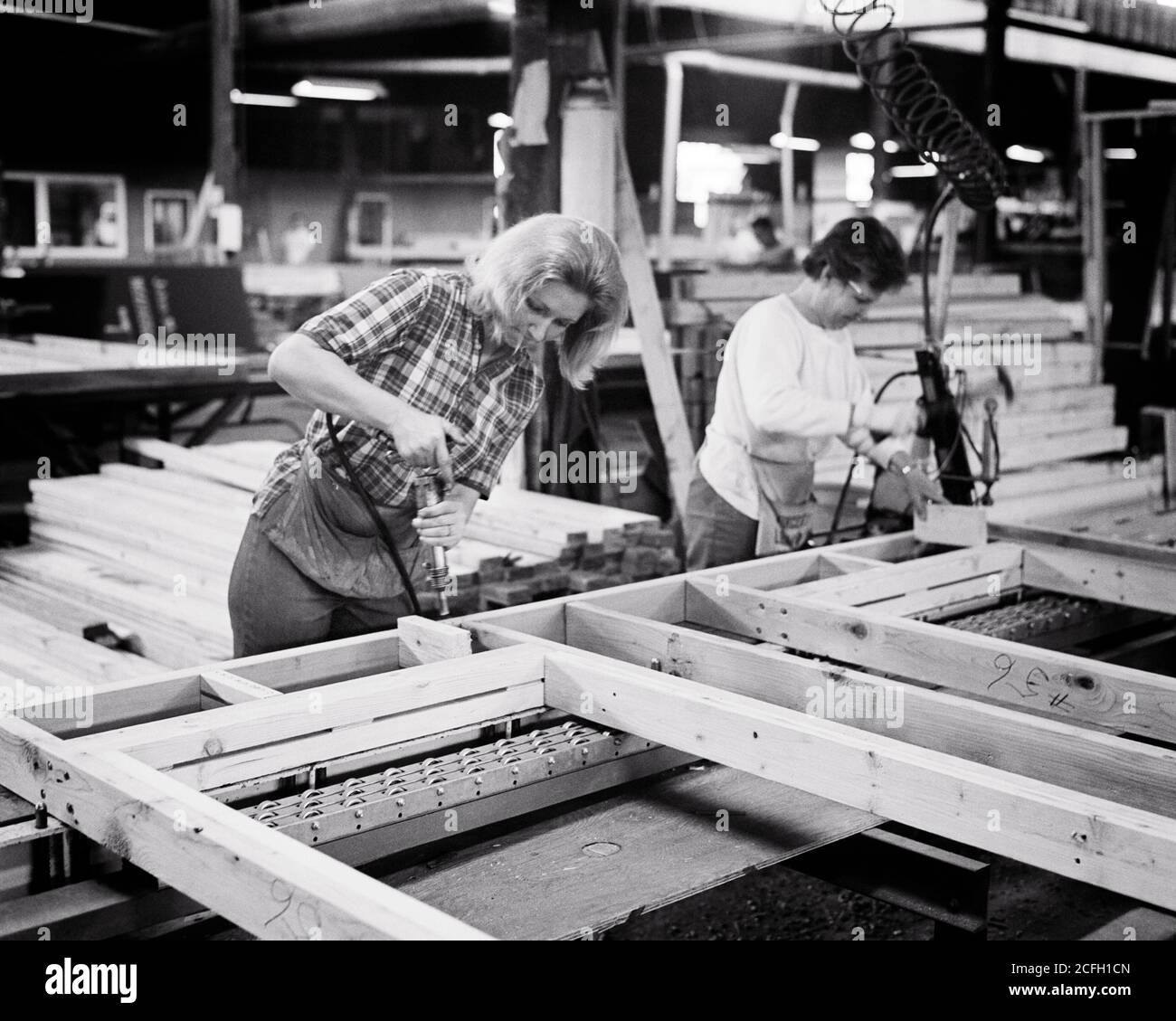 1960s 1970s TWO WORKERS WOMEN ON PREFAB FACTORY FLOOR ASSEMBLING A WOODEN FRAME FOR USE IN PREFABRICATED BUILDING  - i5633 HAR001 HARS HALF-LENGTH LADIES PERSONS PROFESSION B&W SKILL OCCUPATION SKILLS EQUAL PAY WOMEN'S RIGHTS CAREERS ASSEMBLING INNOVATION LABOR EMPLOYMENT OCCUPATIONS EQUAL RIGHTS EMPLOYEE PREFAB EQUALITY MID-ADULT MID-ADULT WOMAN PRECISION PREFABRICATION USE YOUNG ADULT WOMAN BLACK AND WHITE CAUCASIAN ETHNICITY HAR001 LABORING OLD FASHIONED Stock Photo