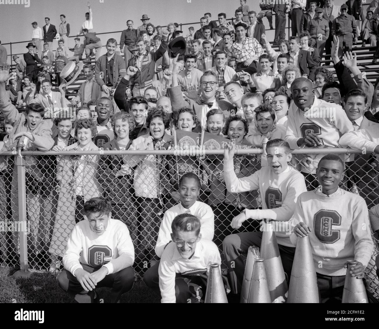 1950s ANONYMOUS HIGH SCHOOL STUDENTS CHEERLEADERS CHEERING SUPPORT FOR THEIR SPORTS FOOTBALL TEAM FROM BLEACHERS STANDS  - j1073 HAR001 HARS OLD FASHION JUVENILE DIVERSE TEAMWORK DIFFERENT PLEASED JOY LIFESTYLE CELEBRATION FEMALES HEALTHINESS COPY SPACE FRIENDSHIP HALF-LENGTH PERSONS INSPIRATION MALES TEENAGE GIRL TEENAGE BOY B&W EYE CONTACT SCHOOLS HAPPINESS CHEERFUL AFRICAN-AMERICANS AFRICAN-AMERICAN EXCITEMENT LEADERSHIP LOW ANGLE RECREATION CHEERLEADERS BLACK ETHNICITY PRIDE HIGH SCHOOL SMILES HIGH SCHOOLS CONCEPTUAL BLEACHERS JOYFUL SUPPORT TEENAGED VARIOUS ANONYMOUS STANDS VARIED Stock Photo