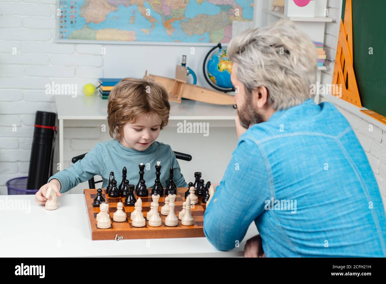 Father and son. Pupil kid thinking about his next move in a game of chess. Dad with his child son are playing Chess. Father and son playing chess. Stock Photo