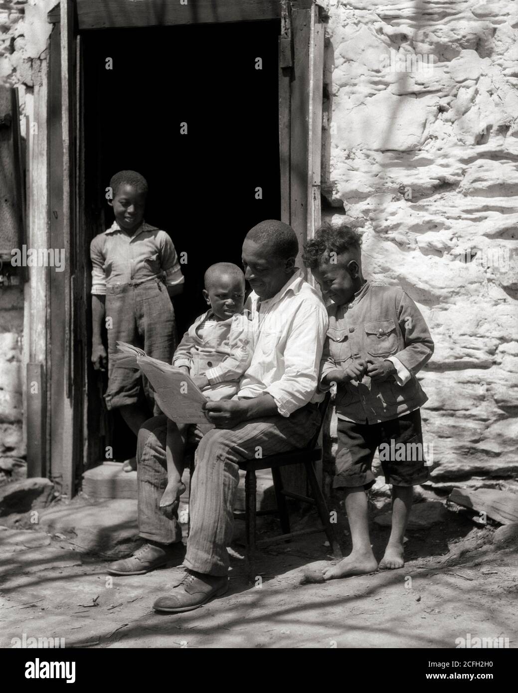 1930s SOLITARY AFRICAN-AMERICAN MAN FATHER SEATED IN BUILDING DOORWAY READING NEWSPAPER SURROUNDED BY THREE BOYS SONS - n947 HAR001 HARS 1 JUVENILE COMMUNICATION INFORMATION SONS FAMILIES LIFESTYLE PARENTING POOR RURAL HOME LIFE SEATED UNITED STATES COPY SPACE FULL-LENGTH PERSONS UNITED STATES OF AMERICA MALES FATHERS B&W NORTH AMERICA NORTH AMERICAN DISCOVERY AFRICAN-AMERICAN DADS SURROUNDED PRIDE BY SOUTHERN CONCEPTUAL DISADVANTAGED SOLITARY GROWTH INEQUITY JUVENILES MID-ADULT MID-ADULT MAN TOGETHERNESS BLACK AND WHITE HAR001 OLD FASHIONED Stock Photo