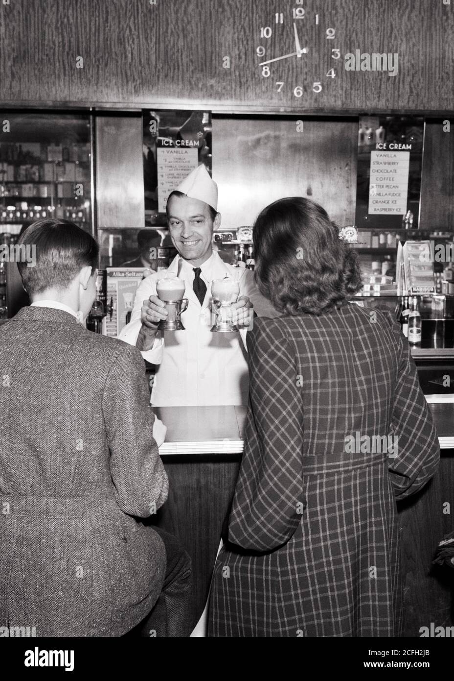 1930s 1940s BACK VIEW TEEN BOY AND GIRL BEING SERVED ICE CREAM SODAS AT FOUNTAIN COUNTER BY SMILING MAN SODA JERK FACING THEM - q40301 CPC001 HARS SUBURBAN SODA URBAN OLD TIME NOSTALGIA OLD FASHION 1 JUVENILE COMMUNICATION YOUNG ADULT PLEASED JOY LIFESTYLE SATISFACTION FEMALES JOBS COPY SPACE FRIENDSHIP PERSONS MALES TEENAGE GIRL TEENAGE BOY CONFIDENCE B&W SKILL OCCUPATION HAPPINESS SKILLS CHEERFUL CUSTOMERS CUSTOMER SERVICE PRIDE REAR VIEW OCCUPATIONS SMILES SODA JERK SERVER FROM BEHIND JOYFUL TEENAGED ICE CREAM BACK VIEW JUVENILES MID-ADULT MID-ADULT MAN YOUNG ADULT MAN BLACK AND WHITE Stock Photo