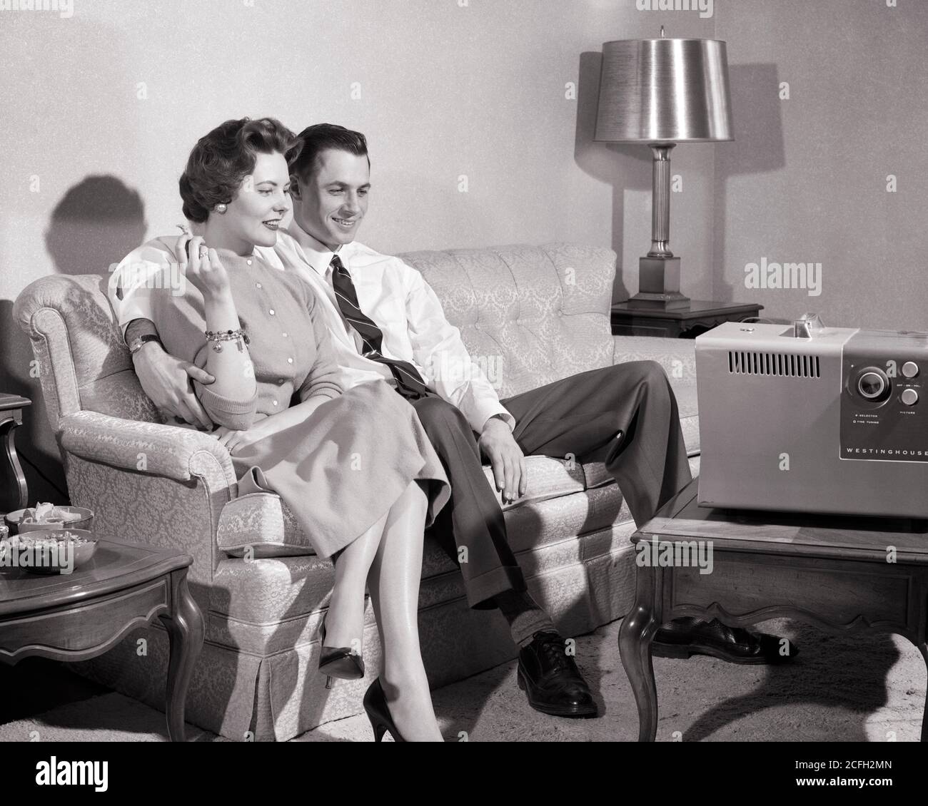 1950s CONTENTED COUPLE MAN WOMAN HUSBAND WIFE SITTING ON COUCH IN LIVING ROOM SMOKING WATCHING PORTABLE TELEVISION SET  - r518 HAR001 HARS COUCH COMMUNICATION PEACE BALANCE INFORMATION PLEASED JOY LIFESTYLE SATISFACTION FEMALES MARRIED SPOUSE HUSBANDS HOME LIFE COPY SPACE FULL-LENGTH LADIES PERSONS MALES ENTERTAINMENT PORTABLE B&W PARTNER WIDE ANGLE DREAMS HAPPINESS CHEERFUL PROTECTION NETWORKING CHOICE EXCITEMENT RECREATION IN ON SMILES CONNECTION ENGROSSED CONCEPTUAL JOYFUL STYLISH CONTENTED MID-ADULT MID-ADULT MAN MID-ADULT WOMAN RELAXATION TOGETHERNESS WIVES ABSORBED BLACK AND WHITE Stock Photo