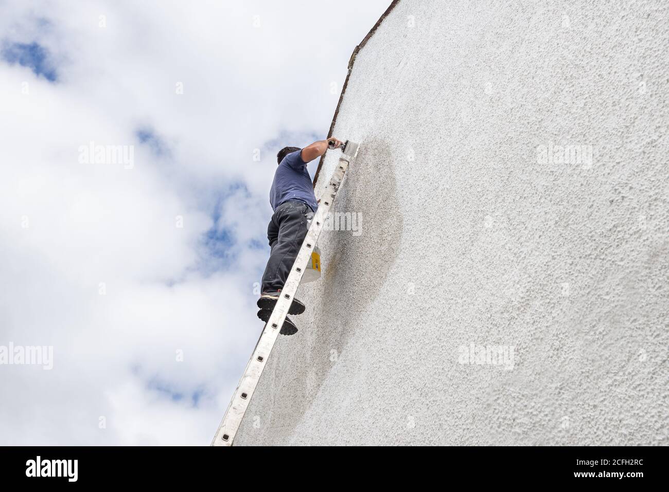 Man up a high ladder painting gable end of pebbledash house. Stock Photo