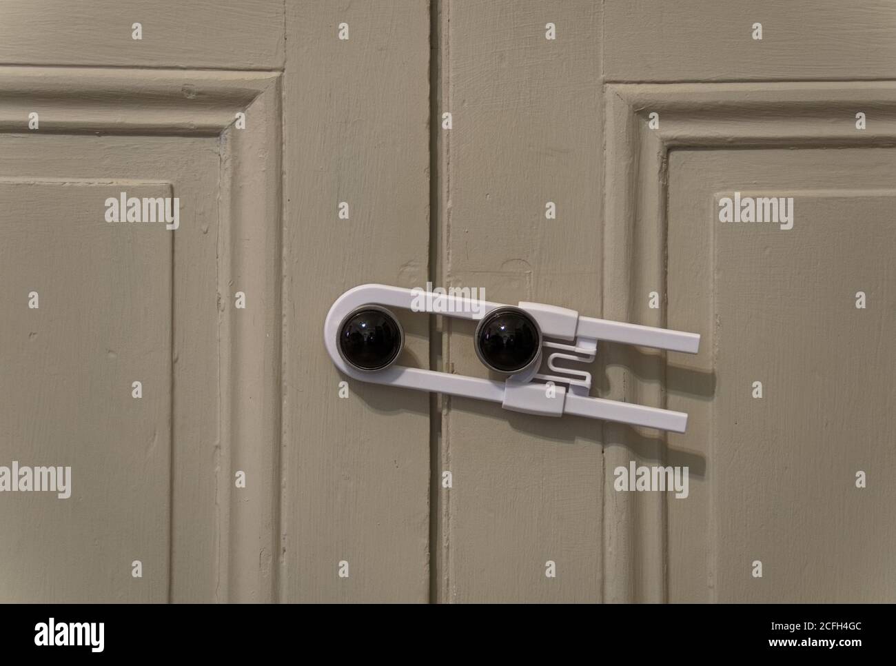 Close up view of a white child safety lock holding two cabinet doors together Stock Photo
