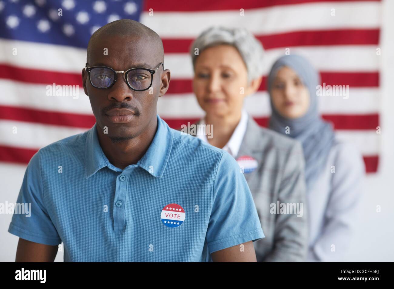 Multi-ethnic group of people at polling station on election day, focus on African-American man with I VOTED sticker looking at camera, copy space Stock Photo