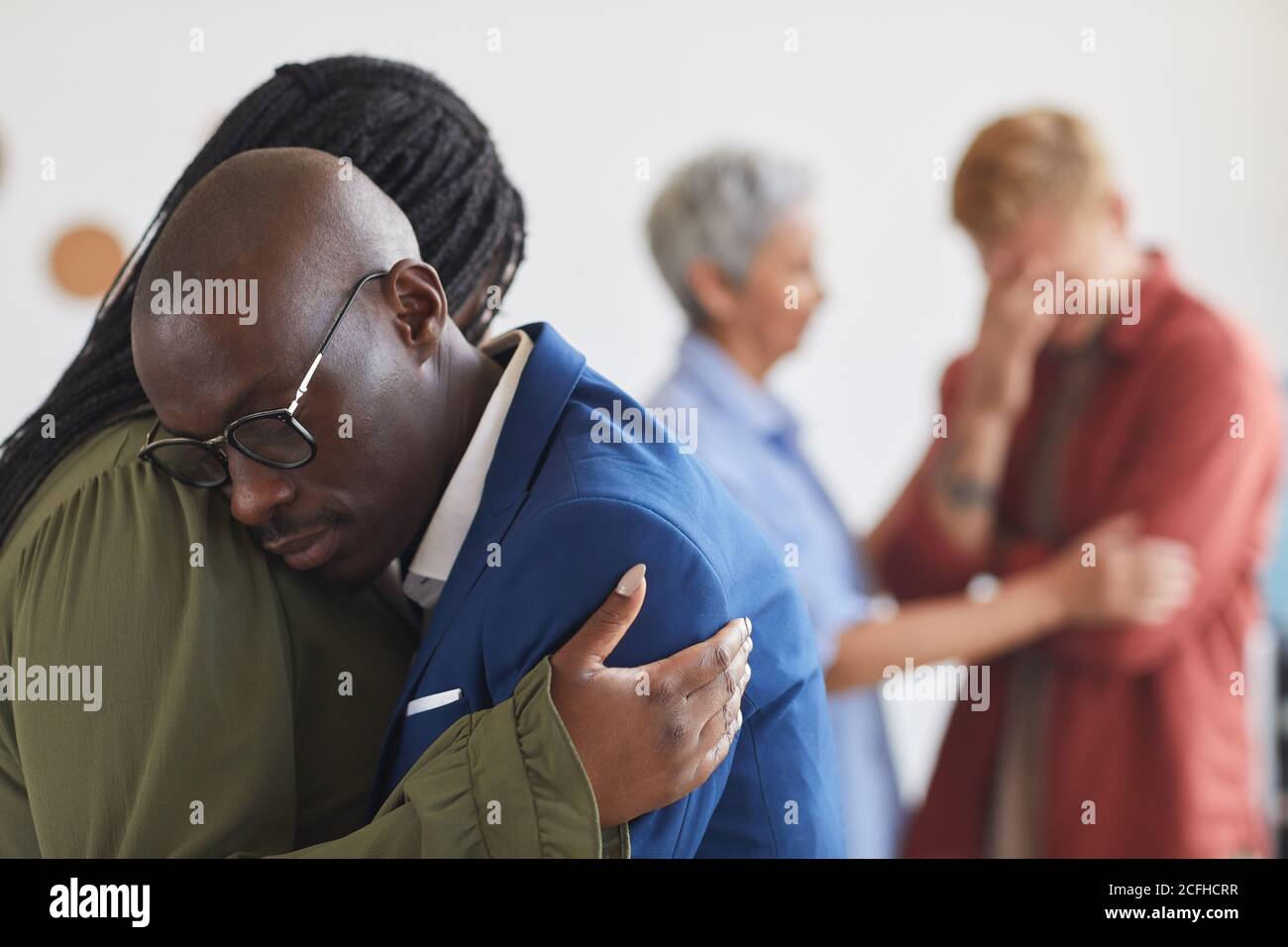 Side view at two African-American people embracing during support group meeting, helping each other with stress, anxiety and grief, copy space Stock Photo
