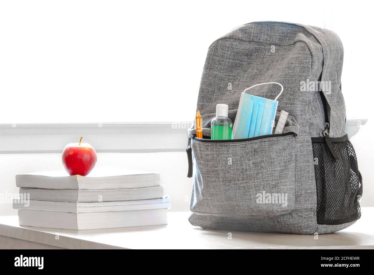Student school bag pack with sanitizer, a face mask, pencils, books and an apple on a table. Back to school during global pandemic. Covid 19. Stock Photo
