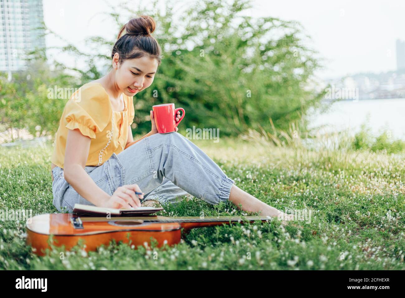 Hands hold coffee cup and write notes,lyrics in the book on quitar beside the sea and building city background. Stock Photo