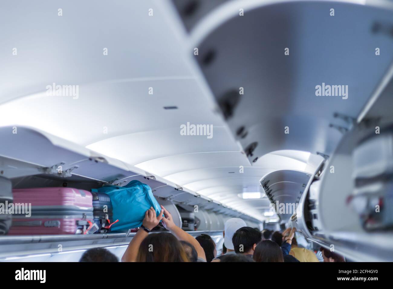 man putting luggage on the top shelf on airplane Stock Photo
