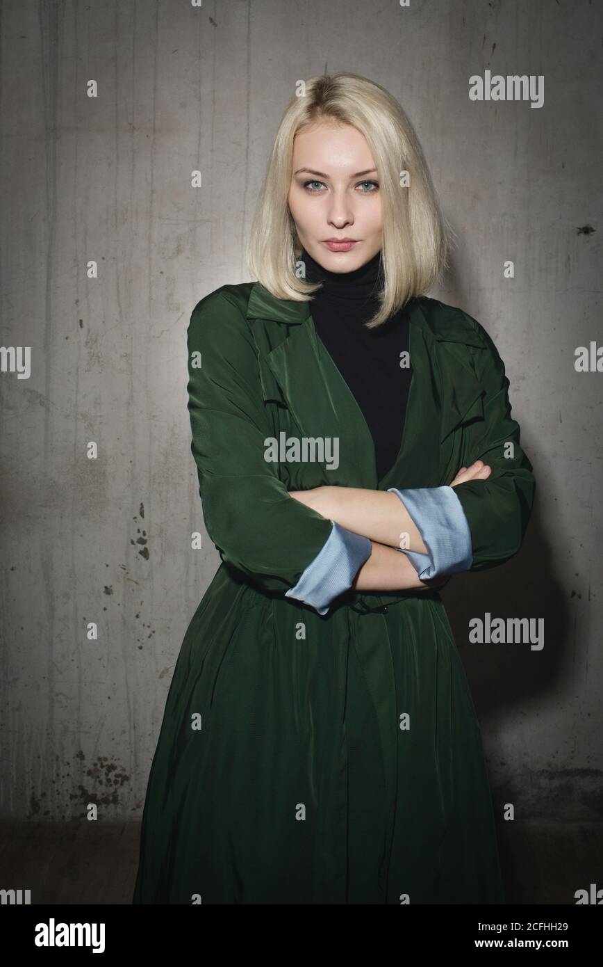 Stylish blonde woman in green coat on background of concrete wall Stock ...