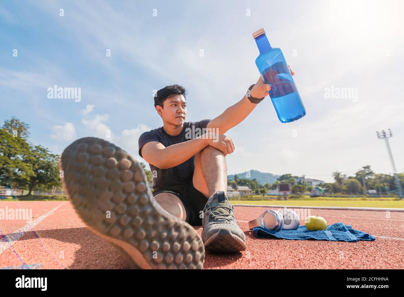Sport man sitting and holding water bottle on track race near green