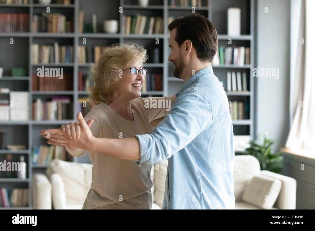 Smiling mature woman dancing with adult son in living room Stock Photo