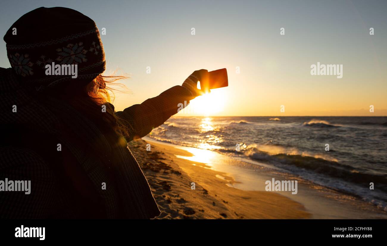 Woman traveler photographs the sea at sunrise on a smartphone camera. Stock Photo