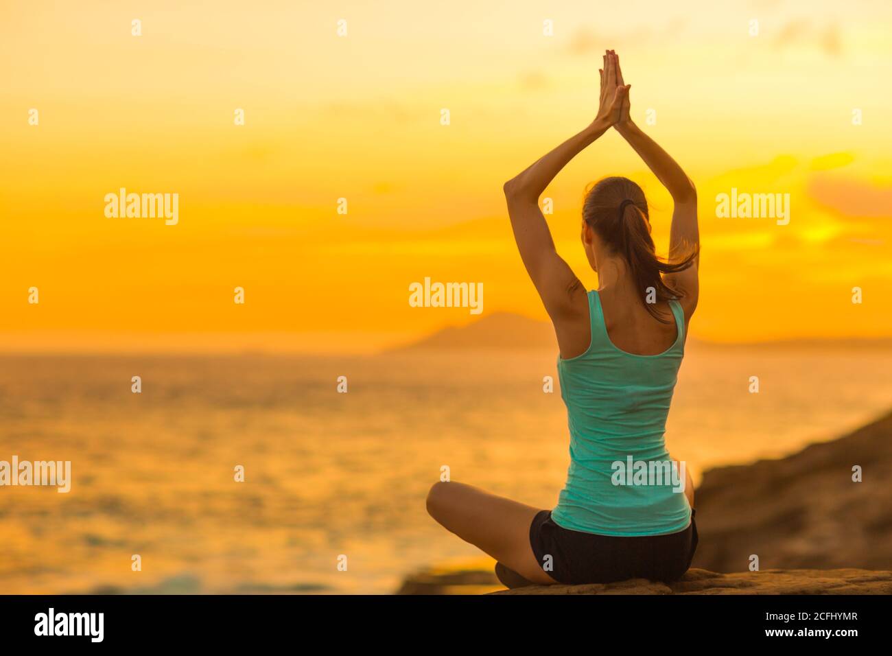 Healthy woman doing yoga meditation exercise at peace on the beach during a beautiful sunset in Hawaii. Body and mind wellness. Stock Photo