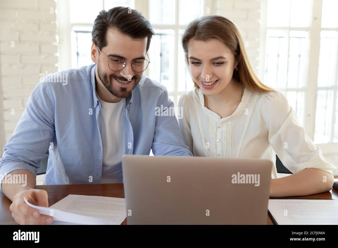 Smiling young man and woman using laptop, checking documents Stock Photo