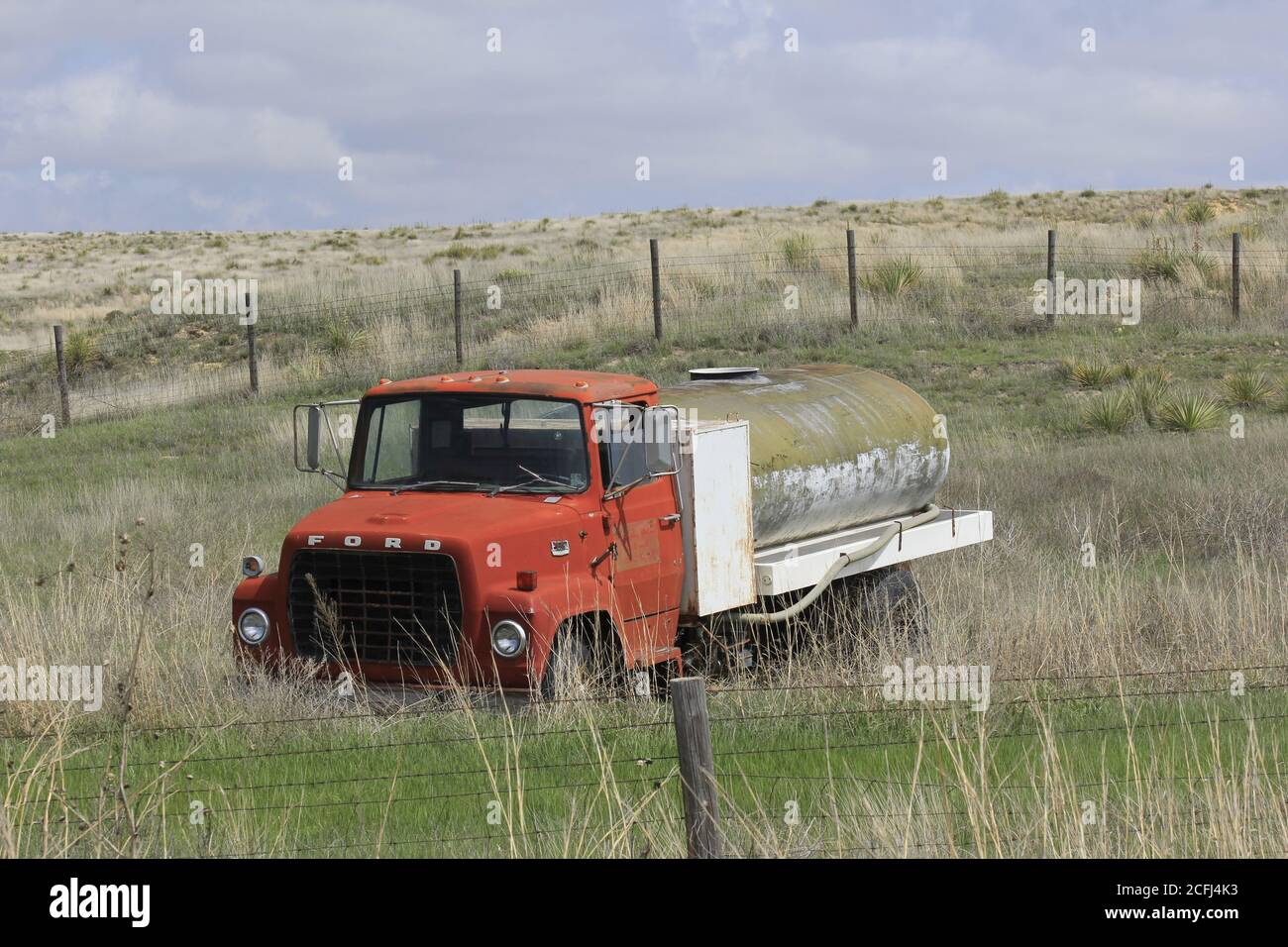 Old Ford Truck water Tanker truck  in a pasture with green grass and a fence in the spring time with blue sky in Kansas. Stock Photo
