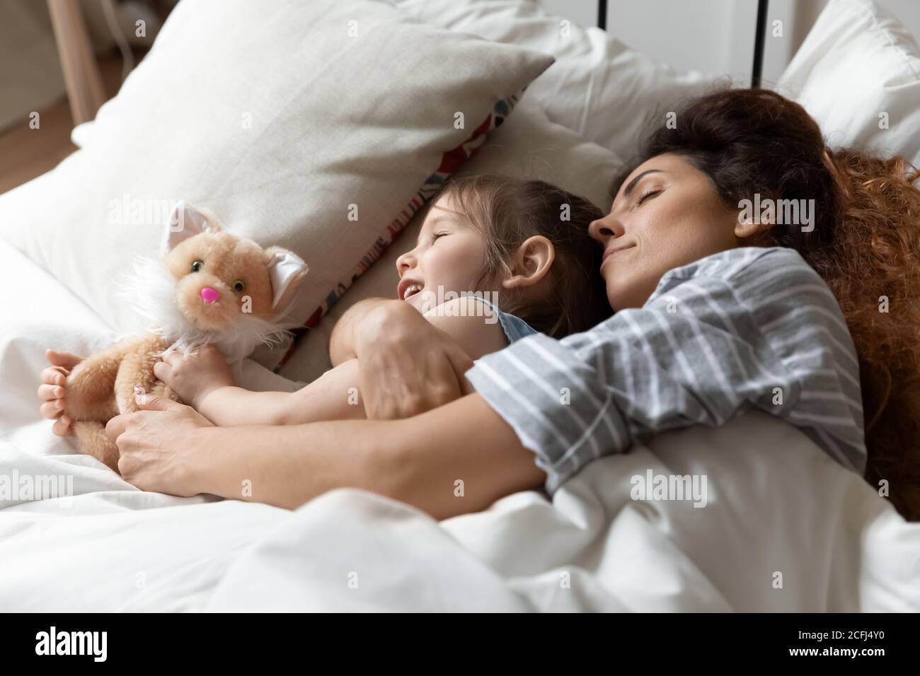 Mommy hug little daughter during daytime nap together in bed Stock Photo