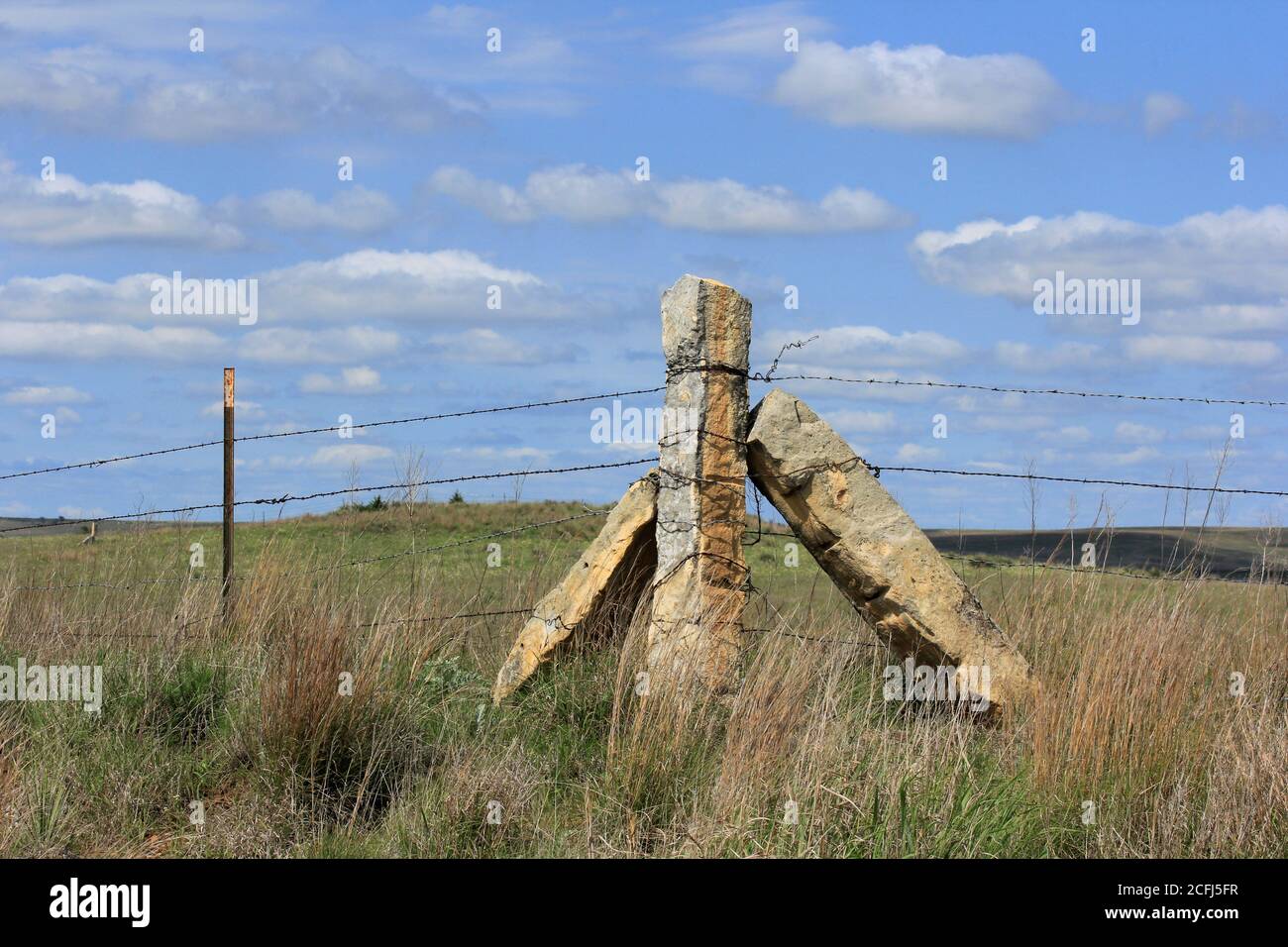 Corner Stone Post  fence in a pasture with prairie grass. With blue sky and white clouds. In Kansas. Stock Photo